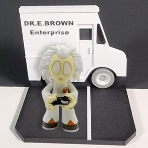 May include: A white toy van with the text "DR. E. BROWN Enterprise" on the side. A small white toy figure of Doc Brown from Back to the Future is standing in front of the van. The van is on a black and white toy street.