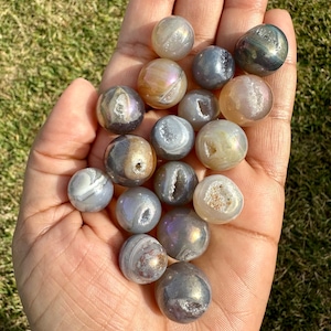 May include: A collection of 15 iridescent agate spheres in various shades of grey, brown, and white. The spheres have a natural, polished finish and feature unique patterns and textures.