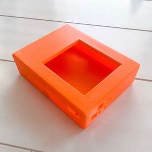 May include: An orange plastic case with a rectangular opening. The case has several small holes on the side.