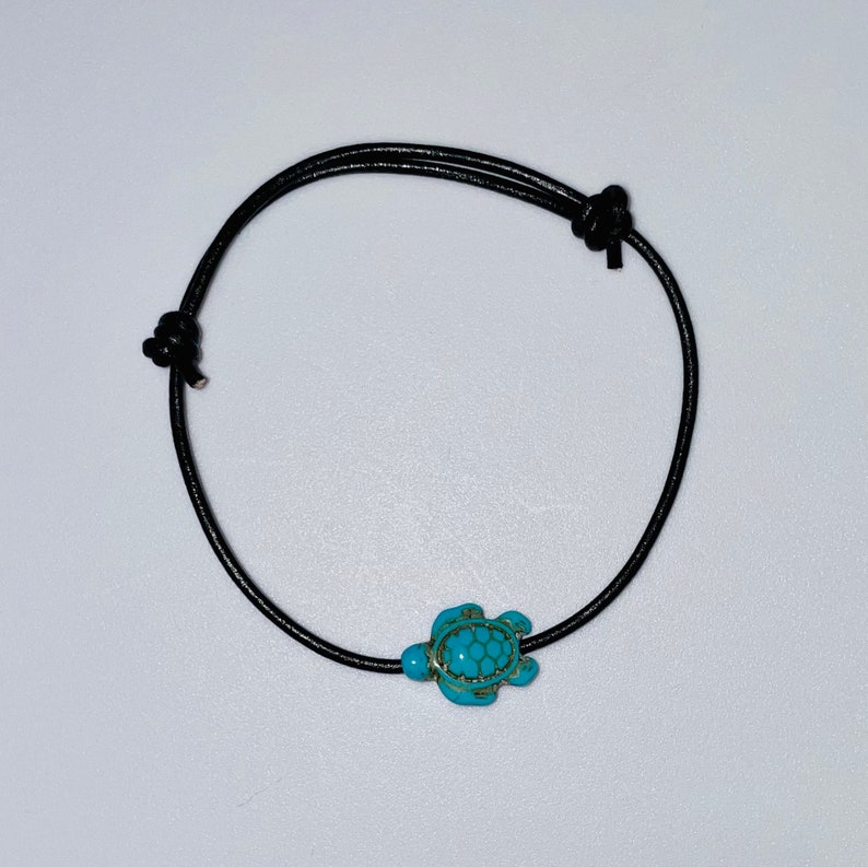 May include: A black leather cord bracelet with a turquoise turtle charm.