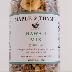 Könnte beinhalten: Ein Glas gefüllt mit einem Granola-Mix namens "Hawaii Mix" von Maple & Thyme. Das Etikett lautet "Unsere einzigartige Mischung aus Ananas, Kokosnuss und Macadamia-Nüssen" und "Handgefertigt in kleinen Chargen". Das Glas enthält 16,5 Unzen (468 Gramm).