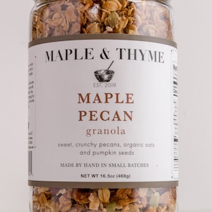 Könnte beinhalten: Ein Glas mit Ahorn-Pekan-Granola. Das Etikett zeigt "MAPLE & THYME" und "MAPLE PECAN granola". Das Glas enthält süße, knusprige Pekannüsse, Haferflocken und Kürbiskerne. Nettogewicht: 468g.
