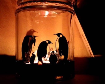 Peut inclure: Un bocal en verre avec une silhouette noire d'une famille de pingouins peinte à l'intérieur. Le bocal est éclairé de l'intérieur, créant une lueur chaleureuse.