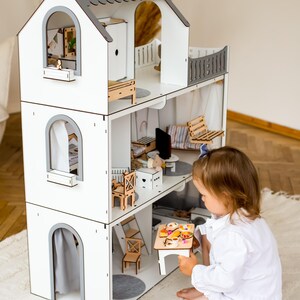A young child is playing with a wooden dollhouse, which is a three-story toy house with various rooms and furniture.