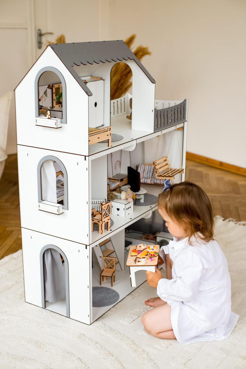 A young child is playing with a wooden dollhouse, which is a three-story toy house with various rooms and furniture.