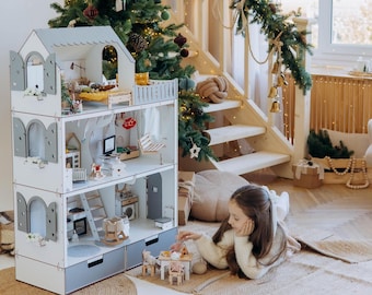 Puede incluir: Una casa de muñecas de madera de tres pisos con un diseño en blanco y gris, ventanas arqueadas con contraventanas y varias habitaciones amuebladas con artículos en miniatura que incluyen una cama, una mecedora, una mesa y una cocina.