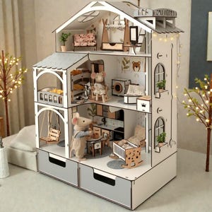 Peut inclure: Une maison de poupée à plusieurs étages avec un extérieur blanc et gris, comprenant des pièces miniatures détaillées avec des meubles et une décoration. Comprend une balançoire, un berceau et une figurine de petite souris. La maison de poupée mesure environ 61 cm de haut.