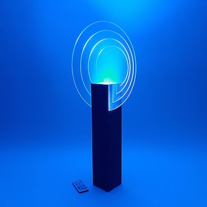 May include: A black cube shaped lamp with a clear acrylic ring that emits blue and green light. The lamp is on a blue surface and has a remote control.