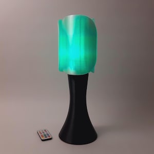 May include: A modern, black and teal lamp with a remote control. The lamp has a unique, curved shade and a wide base.