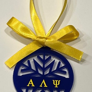 May include: A blue and gold snowflake ornament with the letters "A A Ψ" in gold. The ornament is tied with a yellow ribbon.