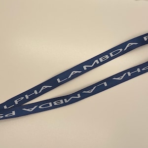 May include: A blue lanyard with a silver clip. The lanyard has the text "ALPHA LAMBDA PSI" printed on it in white.