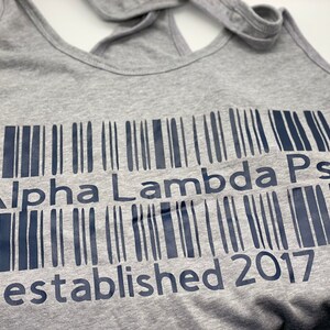 May include: Gray tank top with a black barcode design that reads "Alpha Lambda Psi established 2017".
