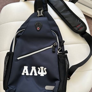 Puede incluir: Una bandolera azul marino con un bolsillo de malla blanca y una cremallera blanca. La bolsa tiene un logotipo blanco que dice "ΑΔΨ".