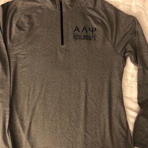 May include: A grey long-sleeved shirt with a zipped neck and the text "&Alpha;&Delta;&Psi; Alpha Lambda Psi" embroidered on the front.