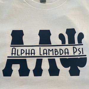 May include: White t-shirt with a black graphic design of the letters "A". "L", and "P" with a black line underneath that reads "ALPHA LAMBDA PSI".