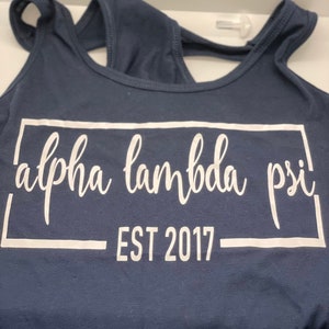 May include: A navy blue tank top with a white graphic that says "alpha lambda psi EST 2017" in a white box.