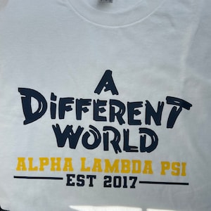 May include: White t-shirt with a navy blue graphic that says "A Different World" and "Alpha Lambda Psi Est 2017" in yellow.