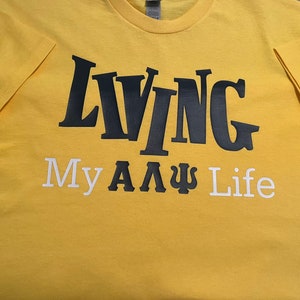 May include: Yellow t-shirt with black text that reads "LIVING My A A Ψ Life".