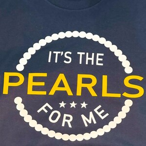 May include: A navy blue t-shirt with a white pearl necklace design and the text "It's the Pearls for Me" in white and yellow.