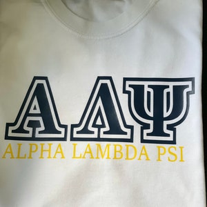 May include: White t-shirt with a navy blue "A A Ψ" design and the text "ALPHA LAMBDA PSI" in yellow.