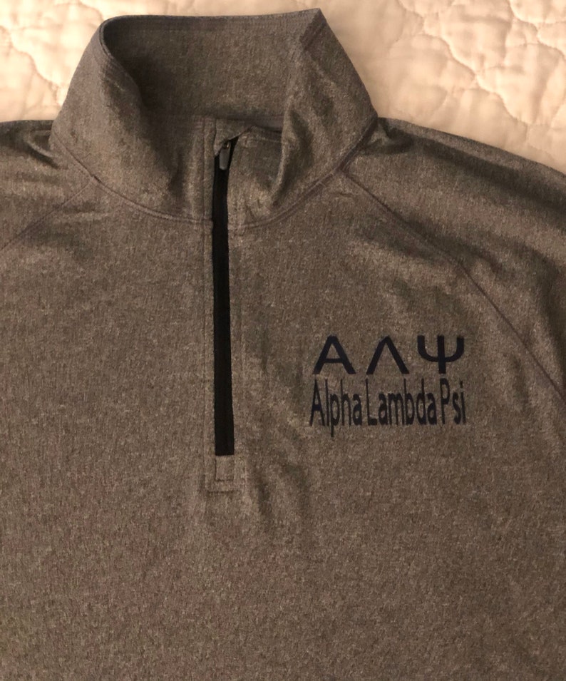 May include: A grey long-sleeved shirt with a black zip and a navy blue embroidered logo that says "&Alpha;&Delta;&Psi; Alpha Lambda Psi".