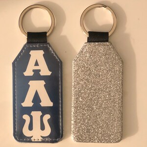 May include: Two keychains, one with a blue leather tag with white letters that say "AA". The other keychain has a silver glitter tag.