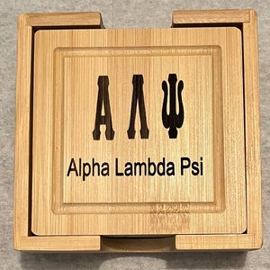 May include: A set of four wooden coasters with a natural wood finish. The top coaster features the letters "A A Ψ" and the text "Alpha Lambda Psi".