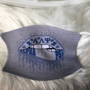 May include: Gray face mask with a blue and white lip design. The lips have the letters "ALPHA PSI" written on them.