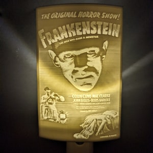May include: A nightlight featuring a vintage movie poster for the horror film "Frankenstein". The poster is in black and white and features a close-up of Boris Karloff as the monster. The text on the poster reads "The Original Horror Show! Frankenstein The Man Who Made A Monster".