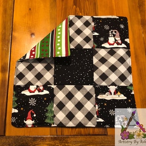 Puede incluir: Salvamanteles de tela a cuadros en blanco y negro con un diseño de patchwork que presenta gnomos, copos de nieve y un búfalo. El salvamanteles tiene un borde a rayas verde, rojo y blanco.