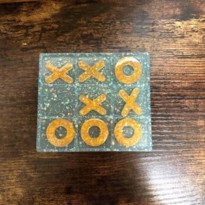 May include: A blue and gold glitter tic-tac-toe game with gold X's and O's.
