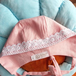 May include: A pink linen baby bonnet with white lace trim and ties. The bonnet has a label that reads "Exclusive Collection".