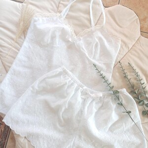 May include: White eyelet camisole and shorts set. The camisole has spaghetti straps and a scalloped lace trim. The shorts have an elastic waistband and a small bow. The set is made of a lightweight, breathable fabric.