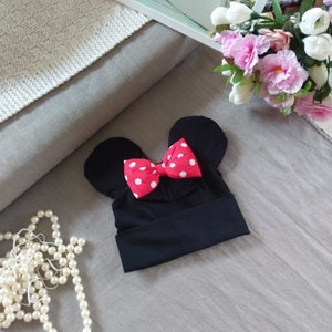 Puede incluir: Sombrero de punto negro con un lazo rojo con lunares blancos en la parte superior, con forma de orejas de Mickey Mouse.