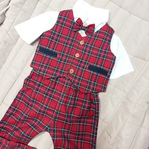 May include: A formal outfit consisting of a short-sleeved white collared shirt, a red and green plaid vest with four light-colored buttons, a matching plaid bow tie, and matching red and green plaid trousers with dark navy blue pocket accents.