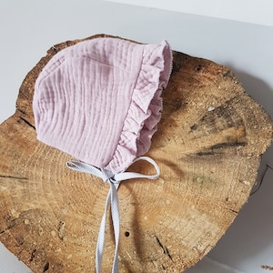 May include: A pale pink baby bonnet with a ruffled edge and a striped ribbon tie.