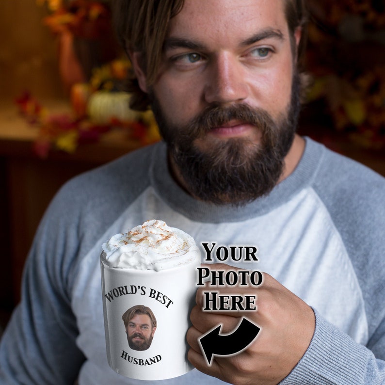 May include: White ceramic mug with a black rim and handle. The mug has a design that says "World's Best Husband" with a space for a photo. The mug is filled with a brown beverage topped with whipped cream and cinnamon.