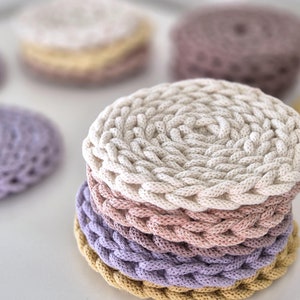 Könnte beinhalten: Ein Stapel aus vier runden gehäkelten Untersetzern in verschiedenen Beige-, Rosa- und Lilatönen. Die Untersetzer bestehen aus dickem, strukturiertem Seil und eignen sich perfekt zum Schutz von Oberflächen vor Hitze und Kratzern.