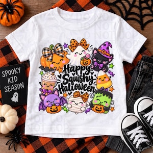 May include: A white short-sleeve t-shirt featuring a colorful graphic print with the text Happy Squishy Halloween. The design includes cartoon illustrations of a pumpkin, ghost, cat, bat, mummy, Frankenstein monster, and candy corn with bows.