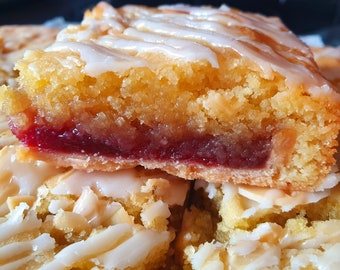 May include: Close-up of a homemade dessert bar with a layer of jam, topped with a white icing glaze. The bar is cut in half, revealing the jam filling.