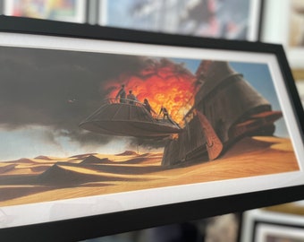 May include: Framed print depicting a desert scene with a hovering craft and figures. A large explosion is visible in the background. The artwork is framed in a black frame with a white mat.