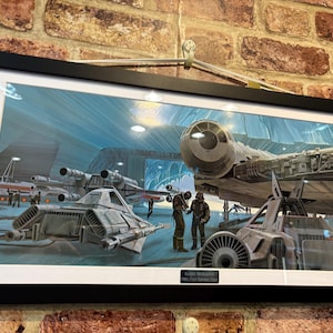May include: Framed artwork showing a science fiction scene with spacecraft in a hangar. The image includes a large, detailed ship and figures in uniforms, enhancing the narrative. The artwork is framed in black, adding a classic touch to the scene.