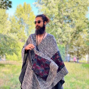 Könnte beinhalten: Ein grauer und schwarzer Poncho mit bunten geometrischen Mustern. Der Poncho ist aus einem weichen, gewebten Stoff gefertigt und hat einen Fransenrand.