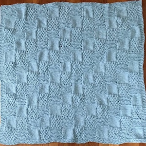 May include: A light blue knitted baby blanket with a checkered pattern.