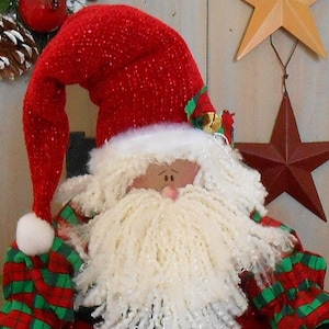 May include: A plush Santa Claus doll with a red suit, hat, and black boots. The doll has a white beard, a painted face, and green and red plaid accents on the sleeves. Gold bells adorn the boots.