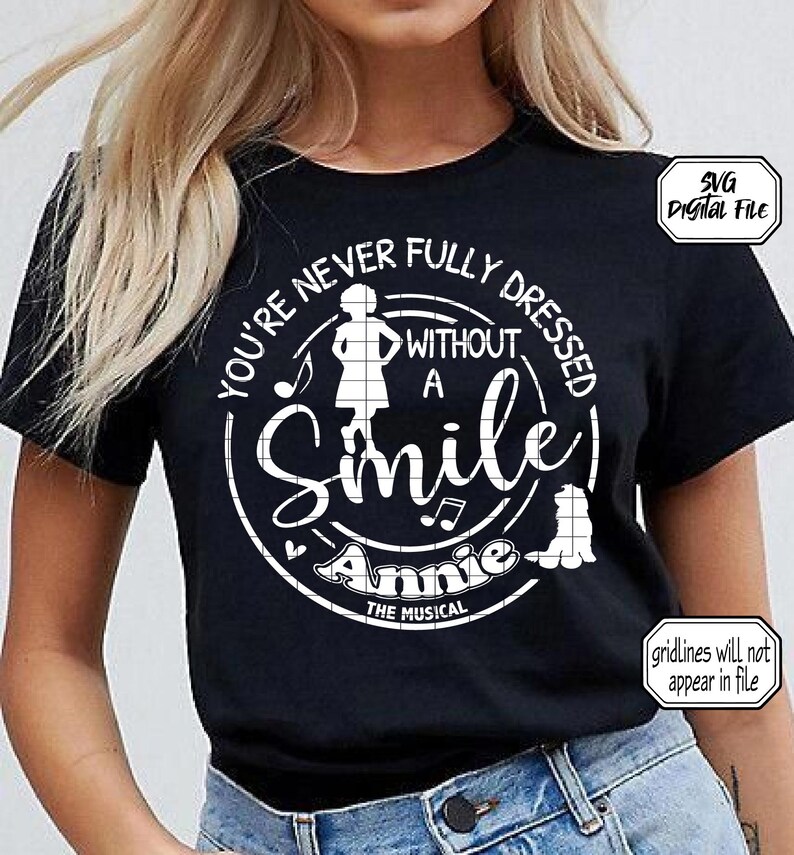 Pu&ograve; includere: Maglietta nera con un design circolare bianco che dice "You're never fully dressed without a smile Annie the musical". Il design include anche una silhouette di una ragazza, note musicali e un cane.
