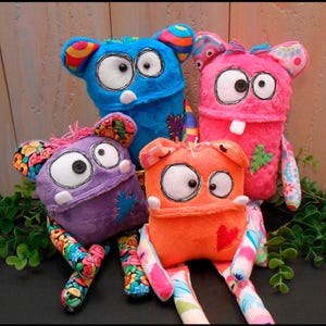 May include: Four colorful handmade monster plush toys. The monsters are blue, pink, purple, and orange, with large white eyes, stitched details, and patterned ears and limbs. Each has a unique stitched patch and a whimsical design.