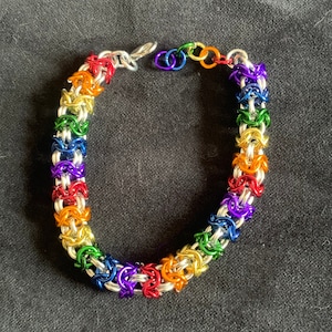 May include: A rainbow coloured chainmail bracelet with silver rings. The bracelet is made with small, interlocking metal rings.