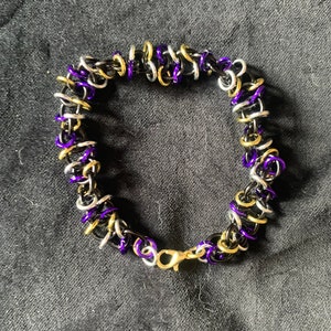 May include: A purple, gold, and silver chain bracelet with a clasp closure.