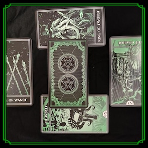 Op de afbeelding: Een spread van tarotkaarten met zwarte en groene illustraties. De kaarten tonen afbeeldingen van de Koning van Zwaarden, De Wagen, Kracht en de 8 van Staven. De achterkant van de kaarten heeft een pentagramontwerp.
